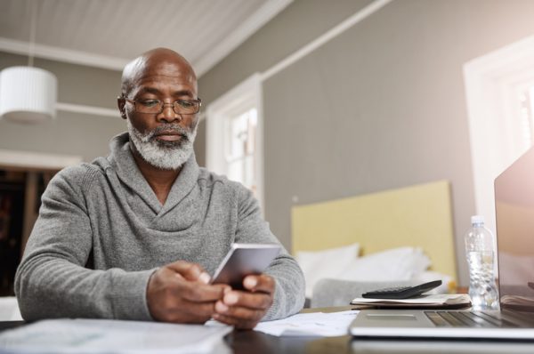 Shot of a senior man using a mobile while working on his finances at home