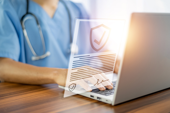 A doctor with a stethoscope sitting in front of.a laptop with a digital cybersecurity certificate