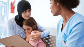 Woman embracing daughter while looking at female nurse holding clipboard - impact of Medicaid cuts.
