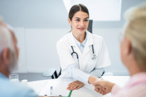 Young female doctor shaking hands with senior couple.