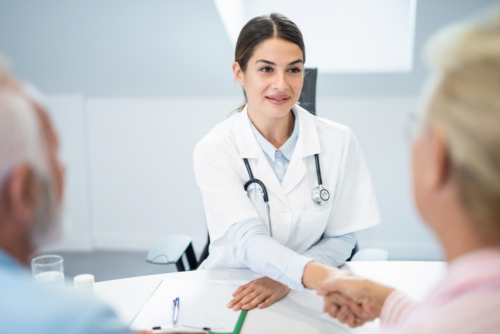 Young female doctor shaking hands with senior couple.