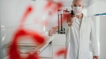 A doctor wearing a mask with a gun pointing straight and a bloody handprint workplace violence