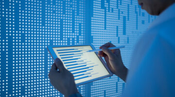 Asian man using tablet in front of a blue screen of data