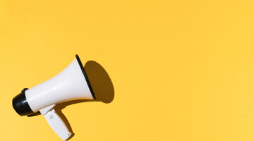 White megaphone with black trim on the left and copy space on the right, on a yellow background. Shout, message, announcement and news concept.