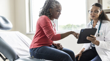 Female doctor and senior woman looking at digital tablet in exam room