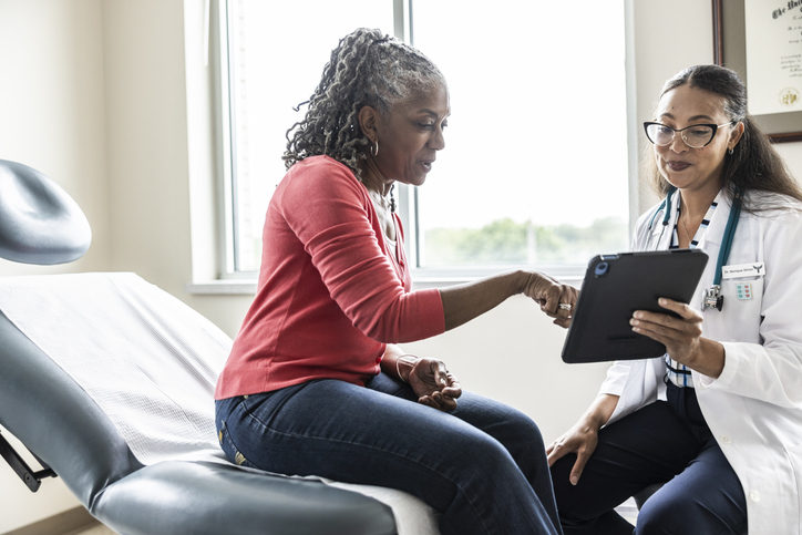Female doctor and senior woman looking at digital tablet in exam room