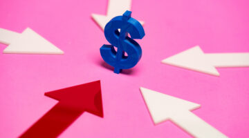 Large blue dollar sign resting on a pink surface, surrounded by white arrows pointing in various directions, with a prominent red arrow directing attention toward the dollar sign healthcare opportunity