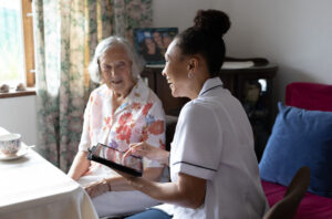 Community nurse using a digital tablet to record details of senior patient