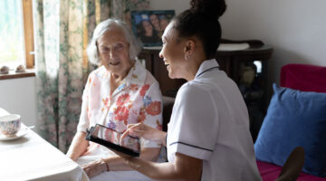 Community nurse using a digital tablet to record details of senior patient