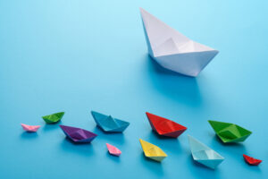 Leadership concept using big white paper ship among other colors on a blue background