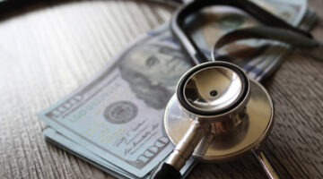 Stethoscope and money on wooden table. Healthcare, medical treatment cost and medicine concept.