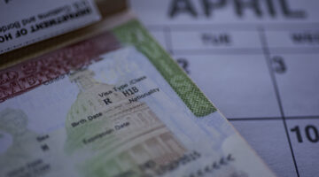 H1B visa (for specialty workers) stamp in passport, blurred april calendar on background. H1B visa program deadline concept. Close up view.