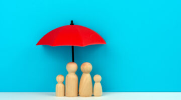 health insurance concept - umbrella covering wooden family of four