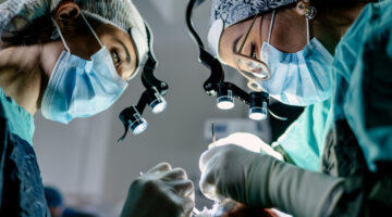 Two surgeons and an instrument technician in an operating room perform reconstructive surgery.