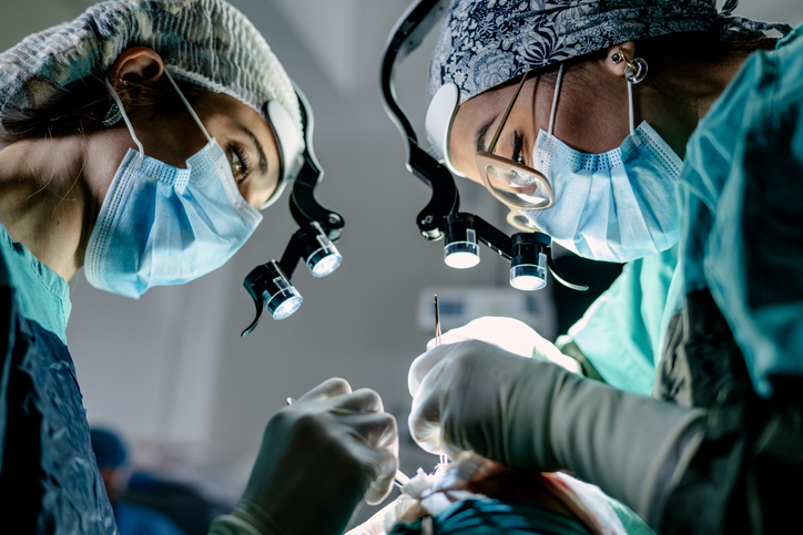 Two surgeons and an instrument technician in an operating room perform reconstructive surgery.