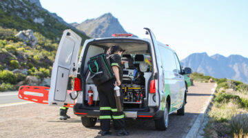 Two caucasian female paramedics wearing protective face masks carrying emergency equipment to an injured hiker on a hiking trial in the Helderberg, Gordon's Bay..