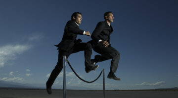 Two businessmen jumping over velvet rope barrier, low angle view