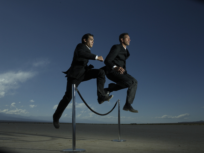 Two businessmen jumping over velvet rope barrier, low angle view