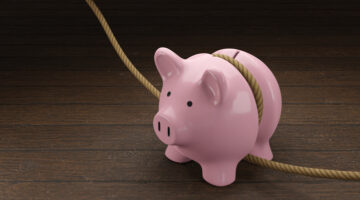 Pink piggy bank is tightened by a rope on wooden table. Illustration of the concept of budget tightening and reduction of spending