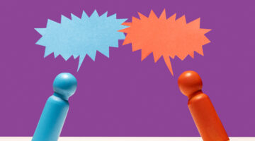 One blue and one red wooden figurine leaning into each other under speech bubbles on white surface, purple background