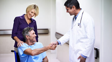 Shot of a doctor shaking hands with a patient in a wheelchair in a hospital corridor while his wife looks on