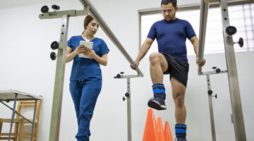 A man exercising with orange cones and a nurse helper showing physical rehab