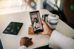 Young adult black woman on a video call with her doctor at home. Telemedicine concept. Over the shoulder view.