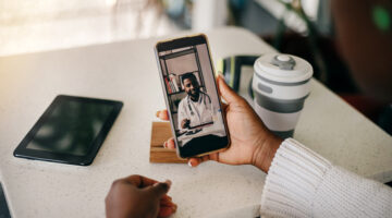 Young adult black woman on a video call with her doctor at home. Telemedicine concept. Over the shoulder view.