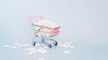 The shopping cart is full of white capsules with medicine and some of the capsules are lying on the floor.