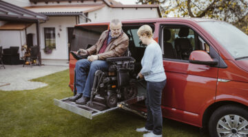 Full length of senior woman holding remote control while helping man with disability in motorized wheelchair to disembar