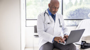 Male doctor working on laptop in exam room