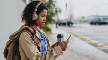 Female nurse, doctor going home from work, waiting for bus, listening music, drinking coffee and scrolling on smartphone. Work-life balance of healthcare worker as parent and partner.