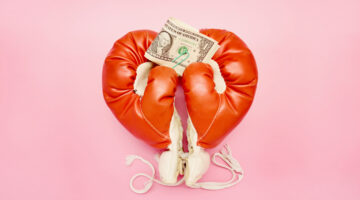 Pair of red boxing gloves in heart shape and American Dollar banknotes on pink background