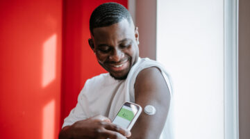 Glucose control. Positive African American man with sensor patch monitor on arm, measuring sugar levels using app