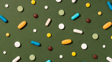 Top view of various colorful pills, capsules and tablets in white, blue, orange, yellow, green and brown scattered on dark green background. Ideal for pharmaceutical editorial, healthcare and medical awareness content, multivitamin or dietary supplement advertising, and drug policy or wellness campaign design