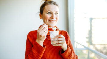 mature woman in an orange sweater enjoys a healthy snack with organic homemade yogurt in a glass by the window in the morning. Authentic moments of real life.