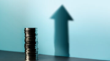 Coins stacked cast a tall upward arrow shadow, reflecting financial growth, profit, and a positive investment direction