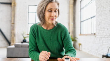Aged healthy woman with wrinkles on the face, dressed in green warm sweater, determines the saturation of the lungs with oxygen, at home, loft style apartment, on the isolation,caring about her health