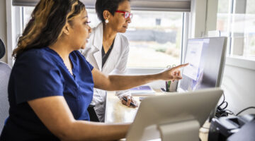 Female doctor and nurse conferring at reception desk in doctor's office